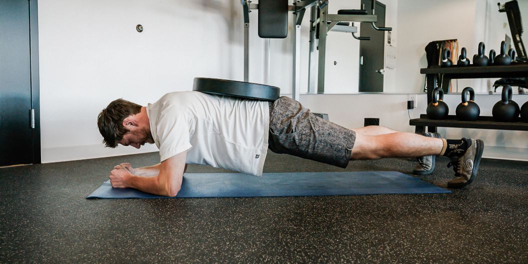 Gym goer performs weighted plank. 